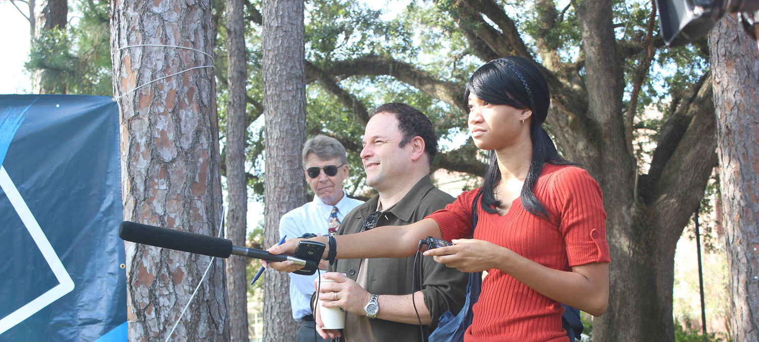 woman holds shotgun microphone towards interview subject off-camera.