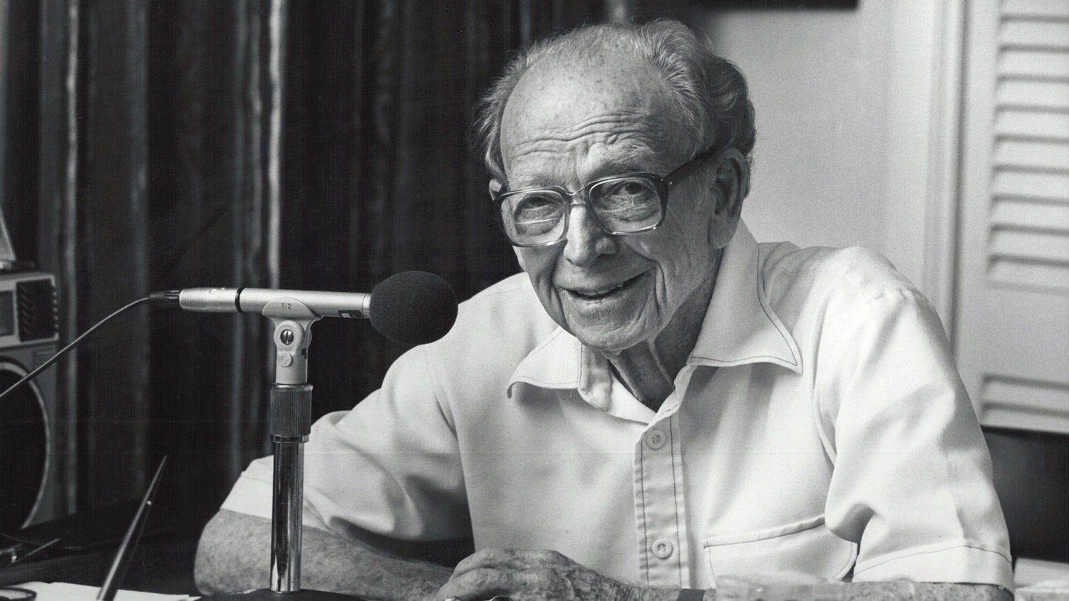 older man sitting at a desk next to a microphone