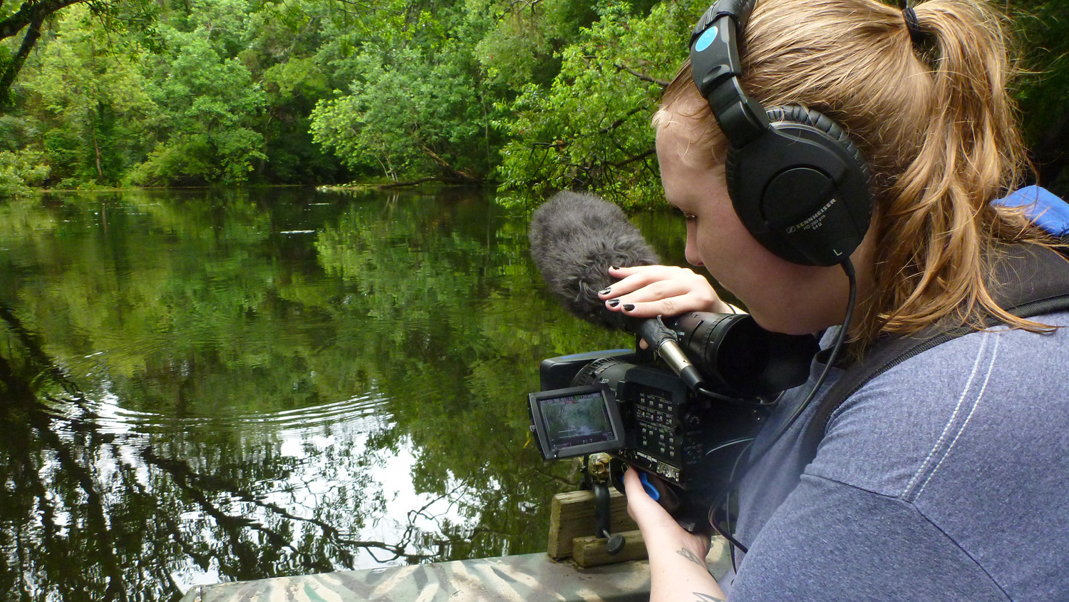 woman with a video camera recording river scenery while on a canoe