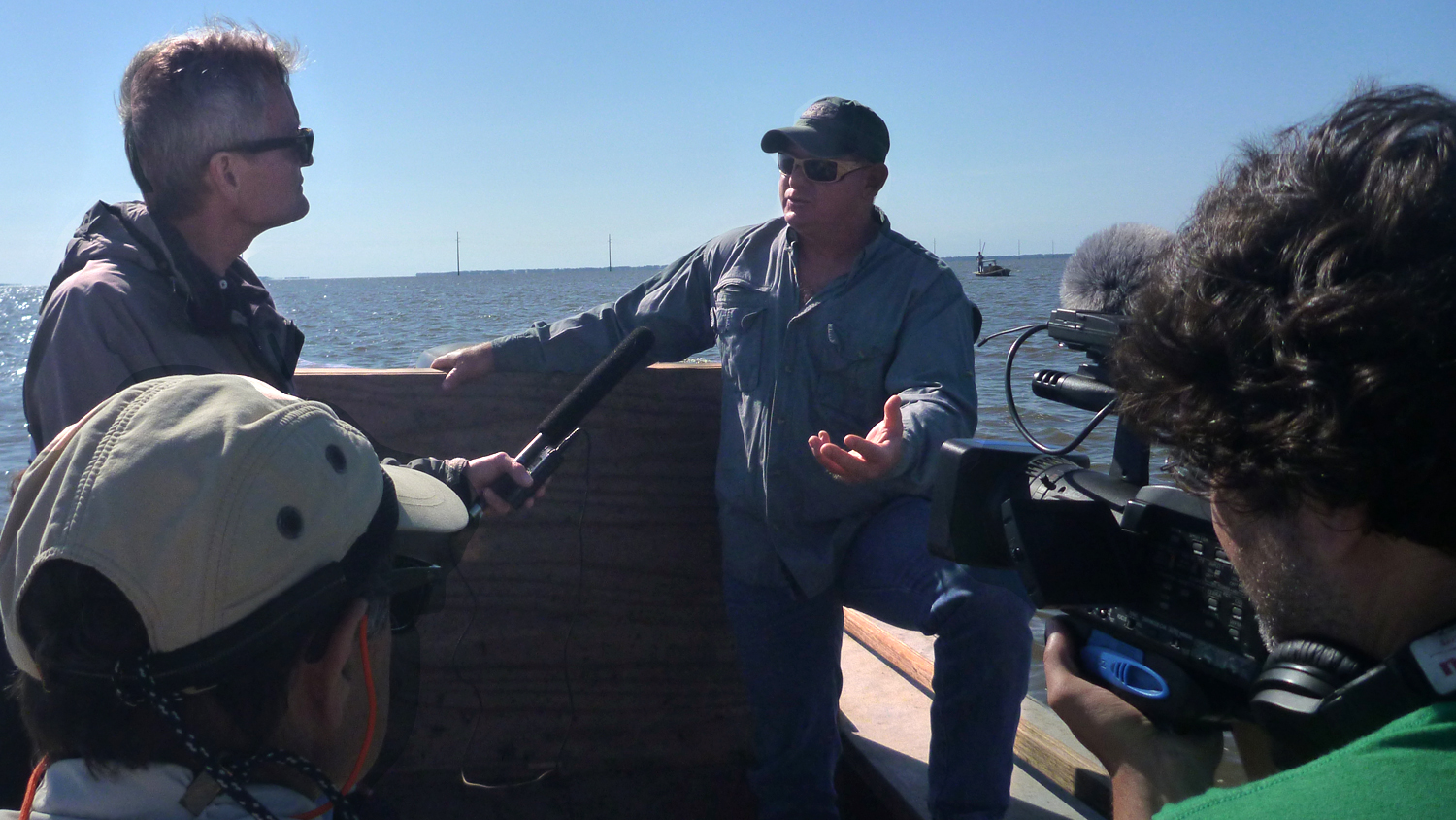 man holding microphone and man holding camera interview oysterman in hat on boat