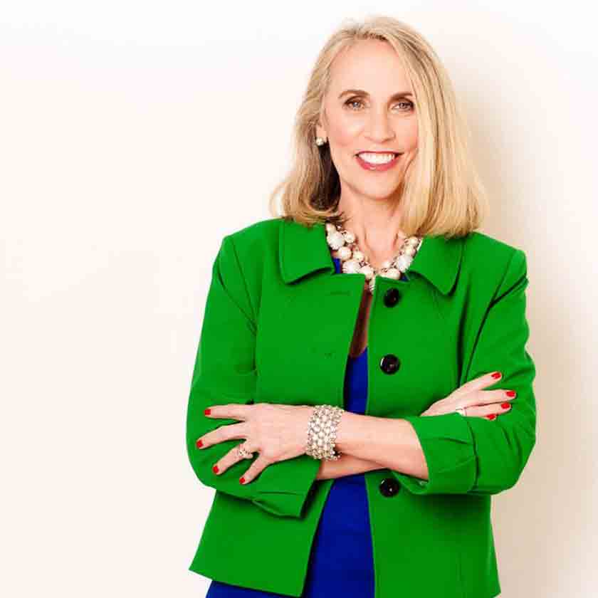 A smiling woman dressed in green and blue stares forward.