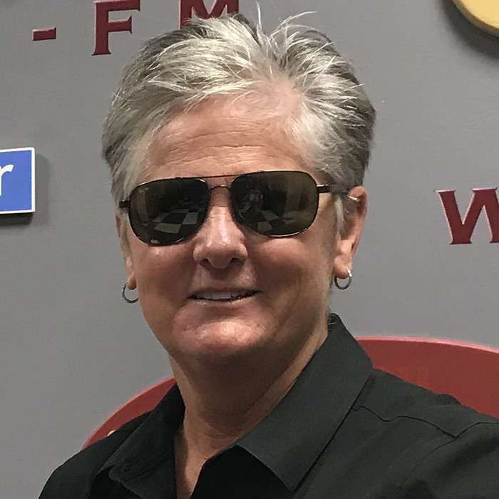 Chief Terri Brown wearing sunglasses in front of the WFSU logos, in the WFSU lobby.