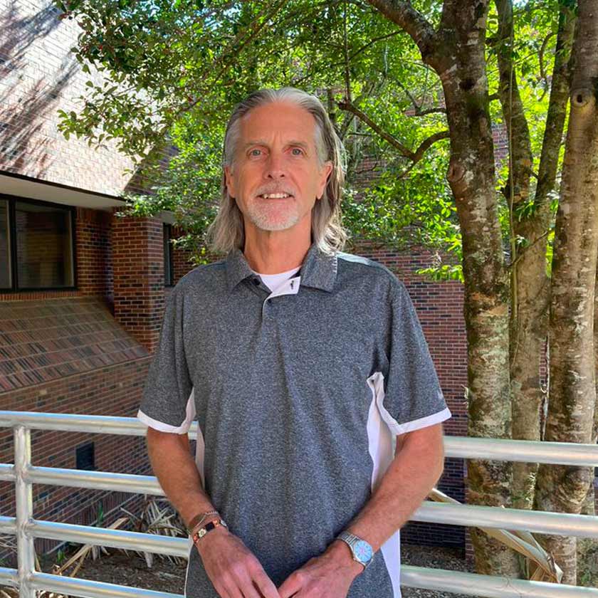 A smiling man stands in front of shrubbery.