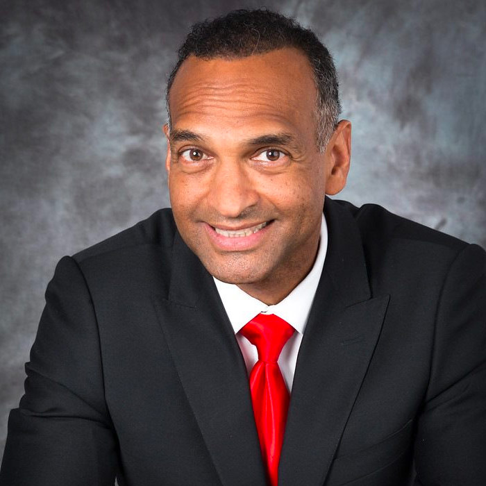 Man smiling in suit in front of grey background.