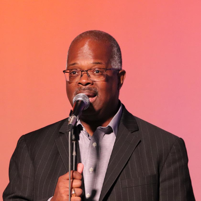 A man in a suit speaks into a microphone.