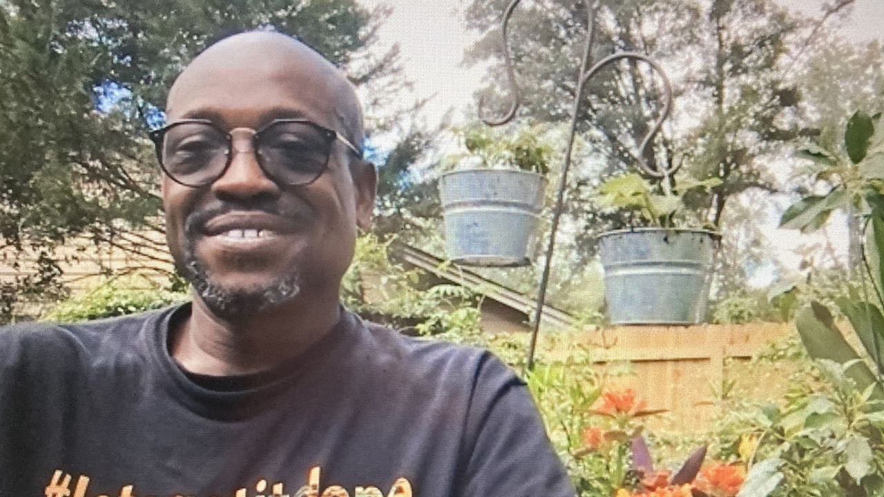 african-american man with glasses sitting in a garden, wearing black t-shirt